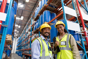 Happy male and female worker looking at camera in warehouse