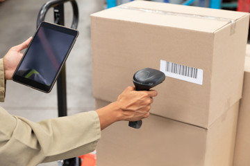 Female worker scanning package with barcode scanner while using digital tablet in warehouse