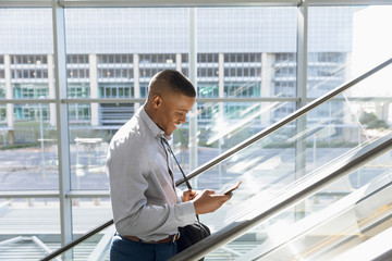 Young businessman using smartphone on an escalator - Powered by Adobe