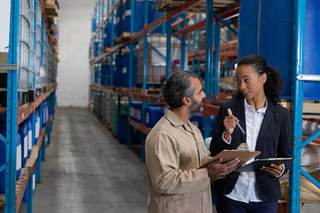 Female manager and male worker discussing over clipboard in warehouse