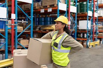 Female staff suffering from back pain while holding heavy cardboard box