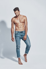 Full length of handsome young shirtless man posing while standing against grey background