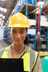 Female staff with clipboard looking at camera in warehouse