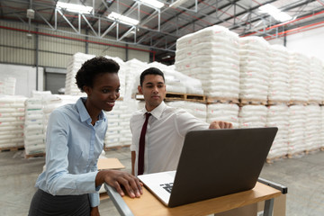 Male and female manager discussing over laptop at desk in warehouse