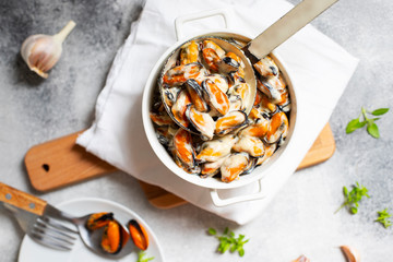 Mussels in cream and white wine sauce. Served with garlic and herbs in a white pan with a ladle....