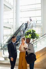 Three diverse young business people talking in the atrium of a modern building