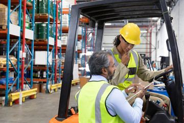 Male and female staff discussing over clipboard in warehouse