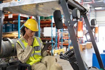 Female staff using digital tablet while sitting on forklift