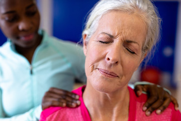 Female physiotherapist giving back massage to active senior woman in sports center