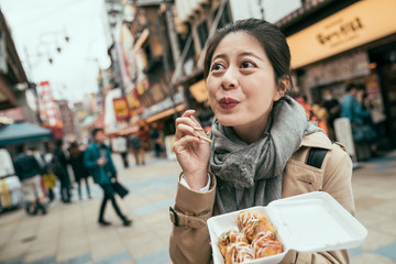 Beautiful asian woman eat takoyaki with lovely smile. cute lady traveler visit tsutenkaku and enjoy famous local food in osaka octopus balls. happy charming female tourist tasting delicious snack