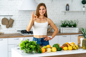 Obraz premium Young woman standing in the kitchen surrounded by mixed fresh vegetables, smiling, looking at camera.