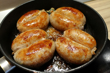 Browned sausages frying on the pan. Octoberfest cuisine objects. Food photography. Juicy and succulent frankfurters. Tasty and appetizing franks