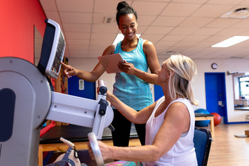 Trainer assisting disabled active senior woman to exercise in exercise equipment