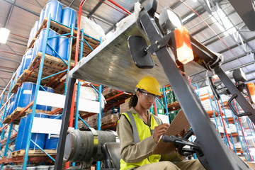 Female staff writing on clipboard while sitting on forklift in warehouse © wavebreak3