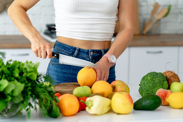 Young beautiful girl cuts fresh orange to prepare fresh juice in the kitchen. Detox diet.