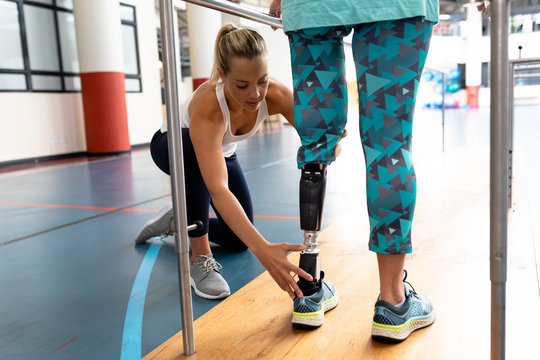 Female physiotherapist helping disabled senior woman walk with parallel bars in sports center