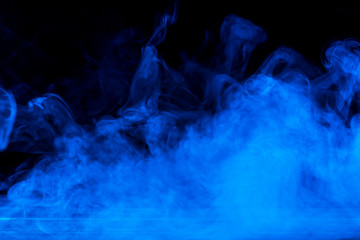 Conceptual image of blue smoke isolated on dark black background and wooden table.