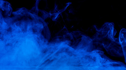 Conceptual image of blue smoke isolated on dark black background and wooden table.