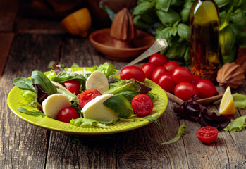 Green salad with mozzarella, tomato and basil in green plate on a old wooden background.