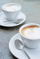 Two cups of cappuccino on a textured grey background. Street cafe. Close-up.
