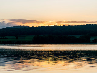 early morning on the lake, dusk, sun rising behind the hill