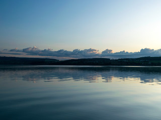 view of the lake at dawn early in the morning, silhouettes of hills and clouds