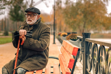 Elderly man sitting in park leaning on cane