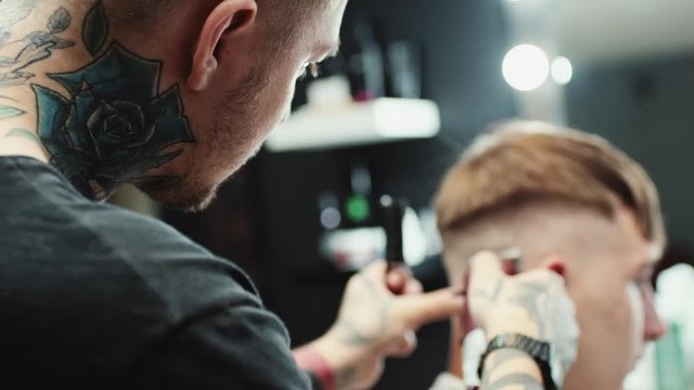 Tattooed barber makes haircut to the client in small barbershop