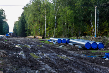 Reconstruction of the gas pipeline . New pipes prepared for installation. Taiga as a background. Excavated soil and traces of construction equipment .