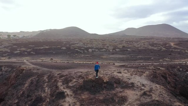 Aerial view of woman in sportswear after jogging stands on top of a rock and enjoys the scenery in a conservation area on the shores of the Atlantic Ocean. Tenerife, Canary Islands, Spain