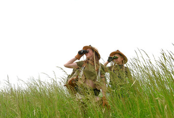 Two young girls dress up as explorers.They pose in  a prairie grassland countryside dressed with jungle  hats and khaki safari clothes.