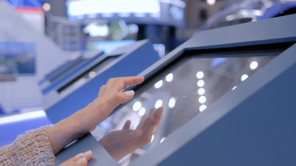 Woman using interactive touchscreen display of electronic multimedia kiosk at technology exhibition - scrolling and touching. Education, learning and technology concept