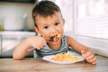a child in a t-shirt in the kitchen eating an omelet with sausage and tomatoes