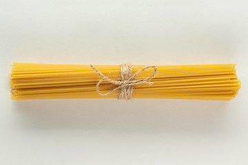 Raw dry spaghetti tied with brown twine on white background isolated