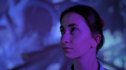 Portrait of woman face looking around at modern immersive exhibition with low light illumination and colorful video art installation. Education, digital art and entertainment concept