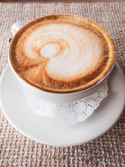 Hot cappuccino with froth and pattern on ackcloth background, a side view