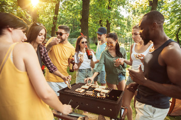 Group of happy friends having beer and barbecue party at sunny day. Resting together outdoor in a forest glade or backyard. Celebrating and relaxing, laughting. Summer lifestyle, friendship concept.