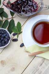 Fresh honeysuckle berries with jam, a cup of tea on a wooden table. Light rustic breakfast.