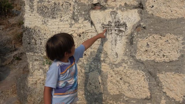 Kayakoy, Fethiye, Turkey - 12th of June 2019: 4K Child points with his finger on a cross on the wall