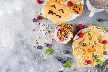 Halloween kids food treat. Funny pancakes - ghosts, jack o Lantern pumpkins, spider webs. Breakfast snack for child's Halloween party, with berries & candy,  gray stone table top view copy space