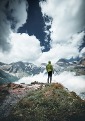 Hiker standing on the Top of a Mountain with Clouds and Fog in the Background. Beauty of nature, tourism and traveling concept