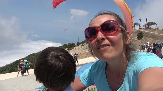1700 m Babadag mountain peak, Fethiye, Turkey - 12th of June 2019: 4K Funny mother and child make selfie at parachute jumping point
