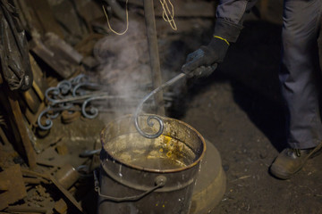 Professional blacksmith working with metal - quenching hot iron part in water at forge, workshop. Handmade, craftsmanship and blacksmithing concept