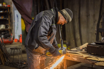 Professional blacksmith sawing metal with hand circular saw at forge, workshop. Handmade,...