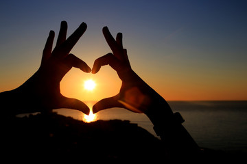 hands in the shape of a heart on the background of the sky let in the sun's rays. On the Sunset. Love concept