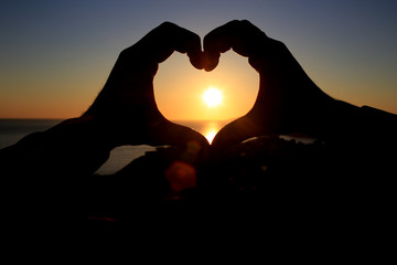 hands in the shape of a heart on the background of the sky let in the sun's rays. On the Sunset. Love concept