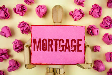 Handwriting text Mortgage. Concept meaning Conditional right of property to lender as warranty from loan written Sticky Note paper holding by Wooden Robot Toy plain background Paper Balls.