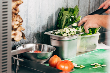 cropped view of cook holding knife at table with cut vegetables