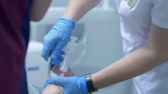 medical procedures, during operation in stomatological office doctor connects an intravenous dropper to a catheter in patients hand