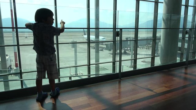 Dalaman Airport, Turkey - 18th of June 2019: 4K Child in waiting watches a plane from airport window